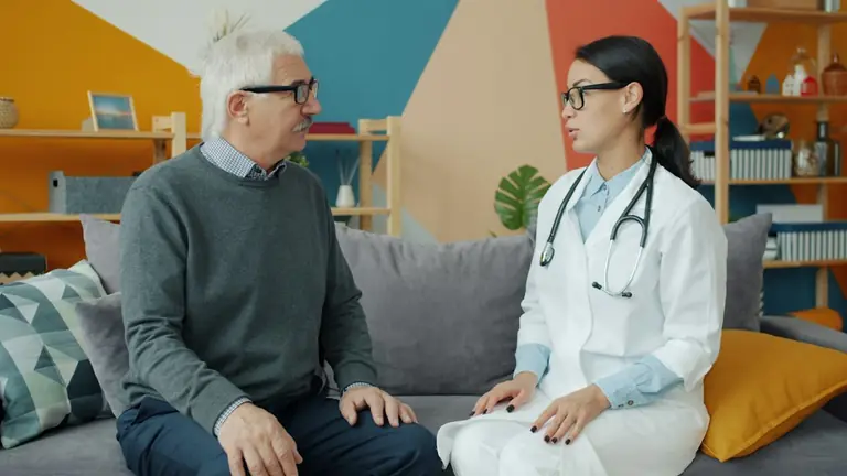 Doctor talks with an elderly patient on a couch.