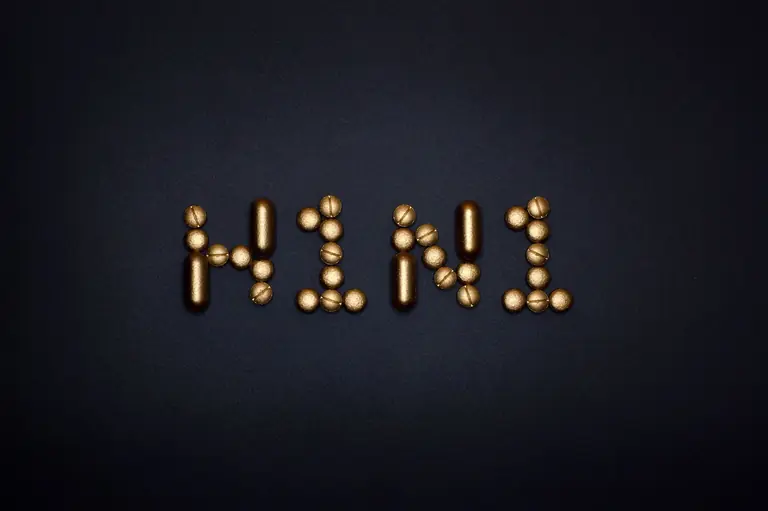 Elegant arrangement of gold pills spelling H1N1 against a black surface, symbolizing healthcare and medication.