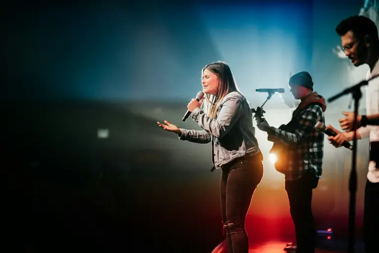 woman in white long sleeve shirt and red pants singing on stage