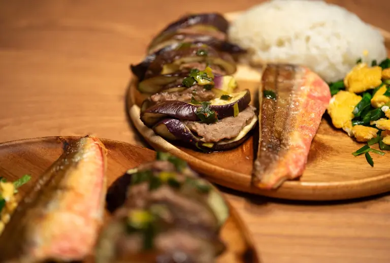 Mouthwatering Asian meal featuring grilled fish, eggplant, and rice on a wooden plate.