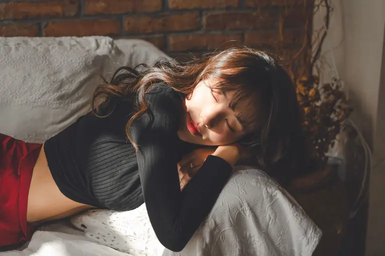 A young woman peacefully resting on a sofa, bathed in warm sunlight indoors.