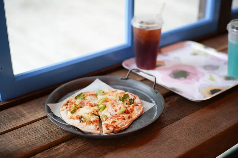 Close-up of a delicious pizza and drinks by a sunny window in a cozy cafe setting.