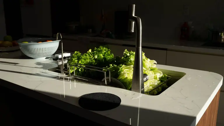 Green lettuce being washed in a modern kitchen sink under sunlight in Hải Phòng, Việt Nam.